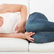 Betroffene von Vulvakrebs Junge Frau liegt auf dem Sofa und leidet an Unterleibsschmerzen.